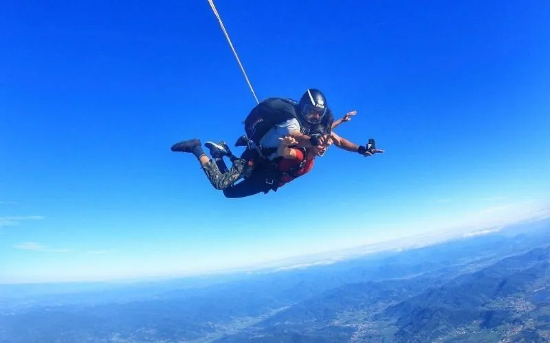 Salto duplo de paraquedas no céu azul, com o litoral lá embaixo