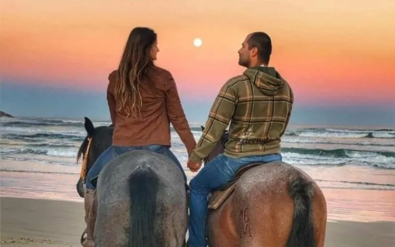 Casal a cavalo na praia ao entardecer