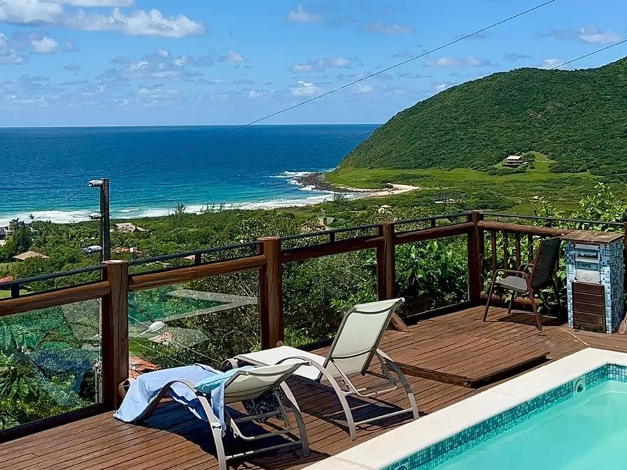 Deck de madeira com espreguiçadeiras, piscina e o mar ao fundo