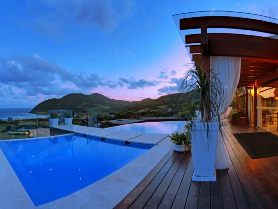 Piscina de borda com vista para o mar e os morros ao entardecer