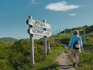 Trilha no campo com placa indicando o caminho da praia