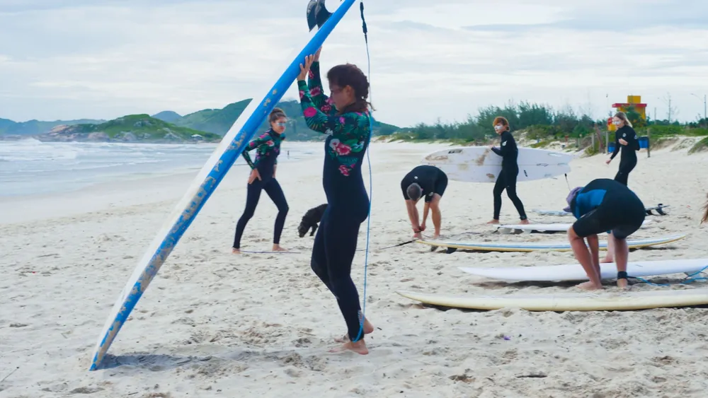 Turma de surf se alongando na areia, com as pranchas