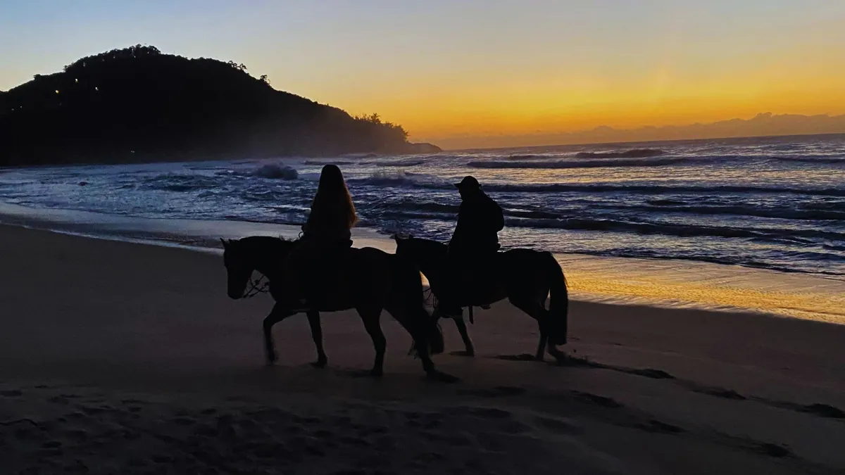 Duas pessoas a cavalo na beira da praia ao pôr do sol